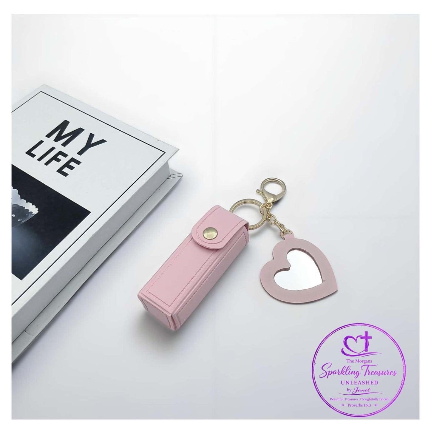 Pink heart-shaped keychain and lip balm case on a white surface with 'My Life' book in the background.