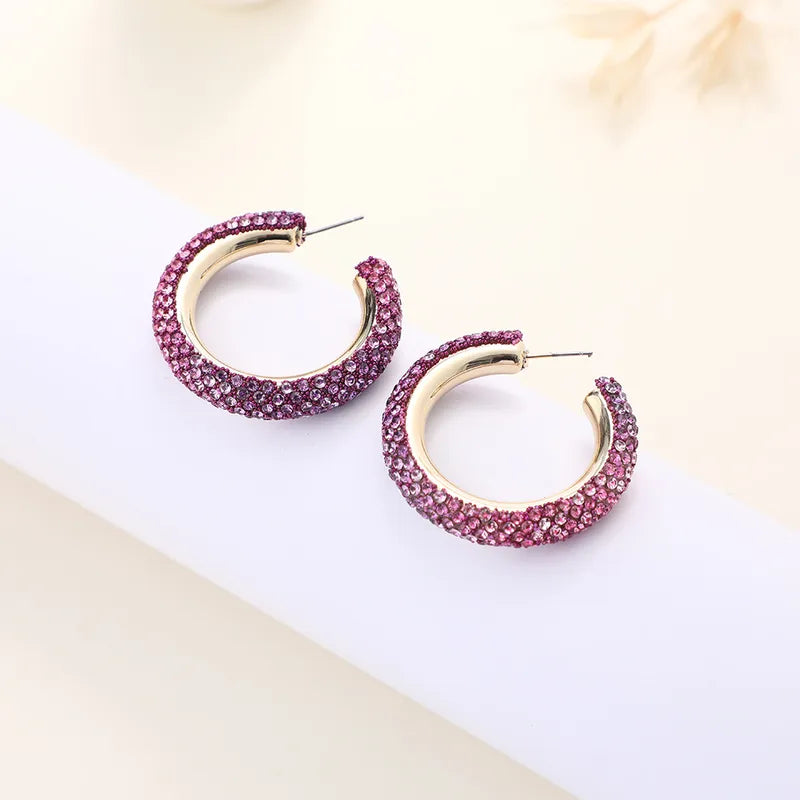 Gold hoop earrings with pink gemstones on a light background