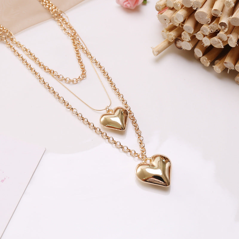 Gold heart-shaped necklace on a white surface with wooden sticks and pink flowers in the background