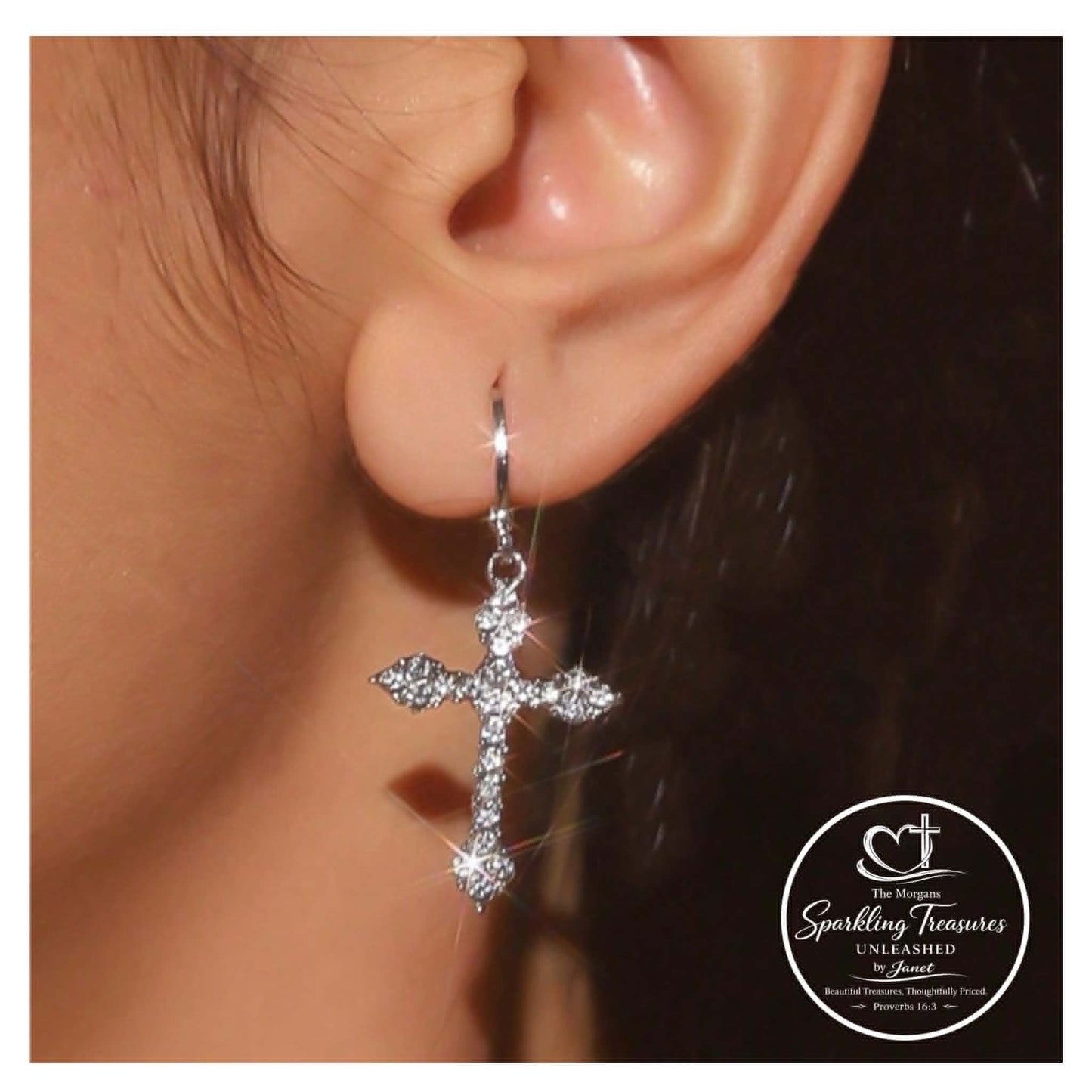 Silver cross earring worn on an ear with a blurred background
