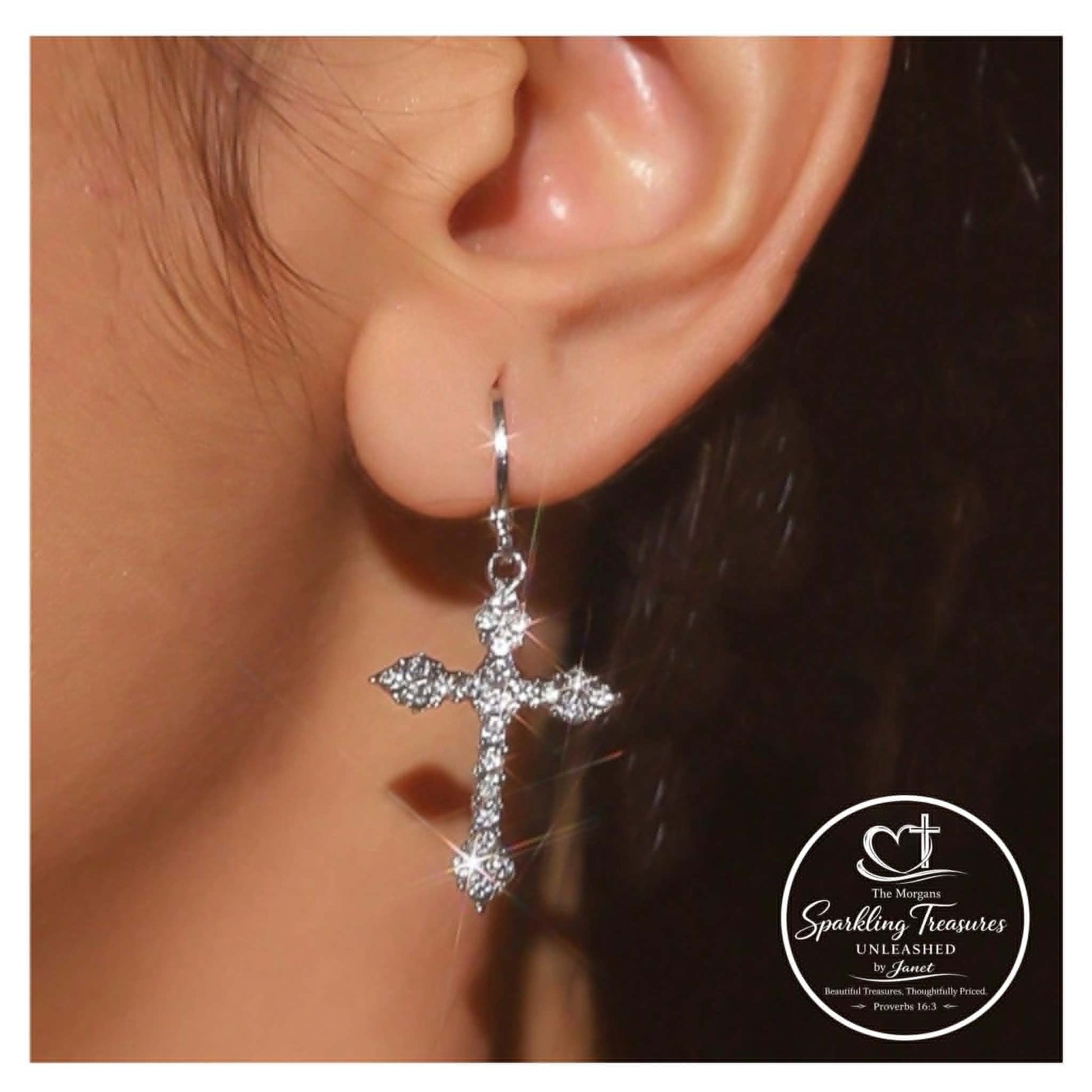 Silver cross earring worn on an ear with a blurred background