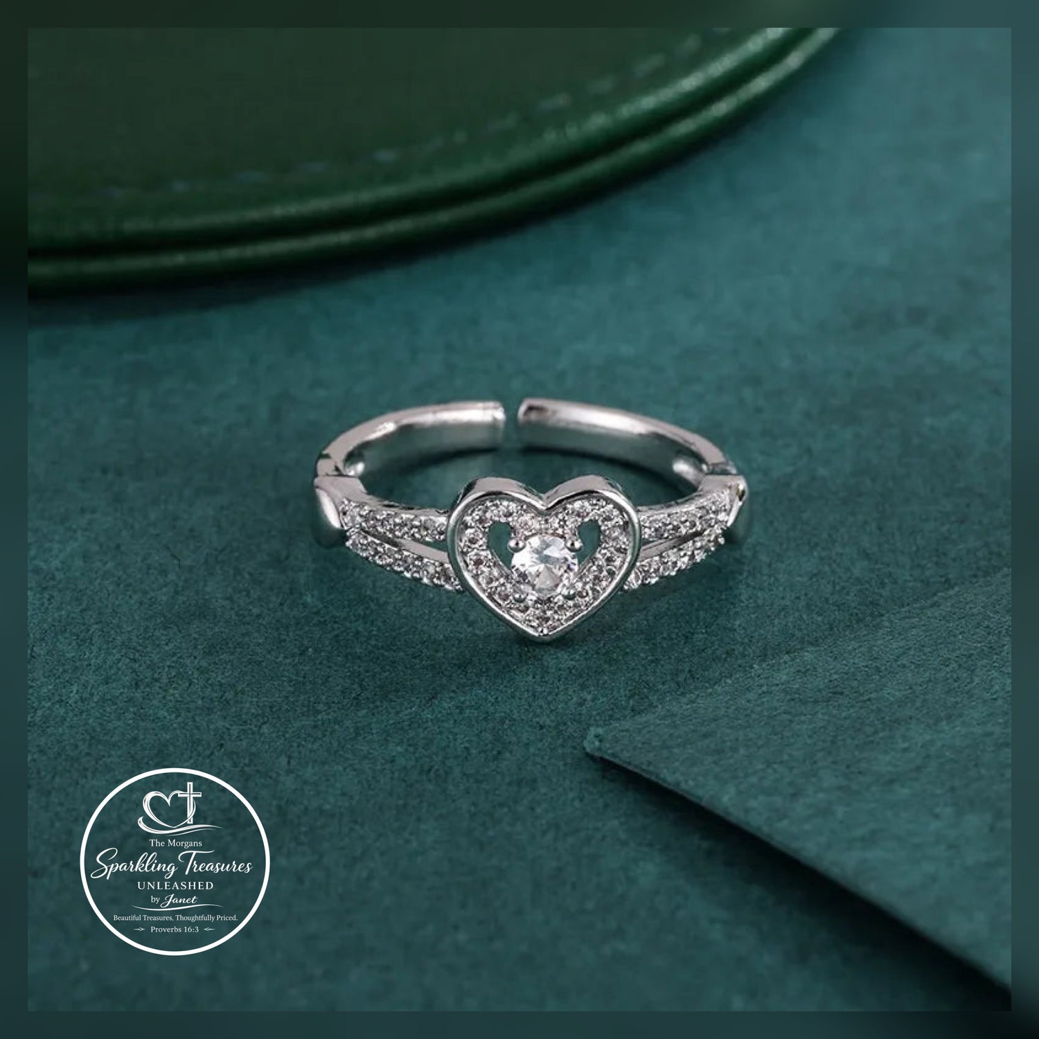 Silver heart-shaped ring with a diamond on a green textured surface, featuring the 'Sparkling Treasures' logo.