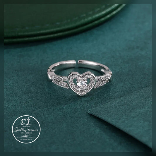 Silver heart-shaped ring with a diamond on a green textured surface, featuring the 'Sparkling Treasures' logo.