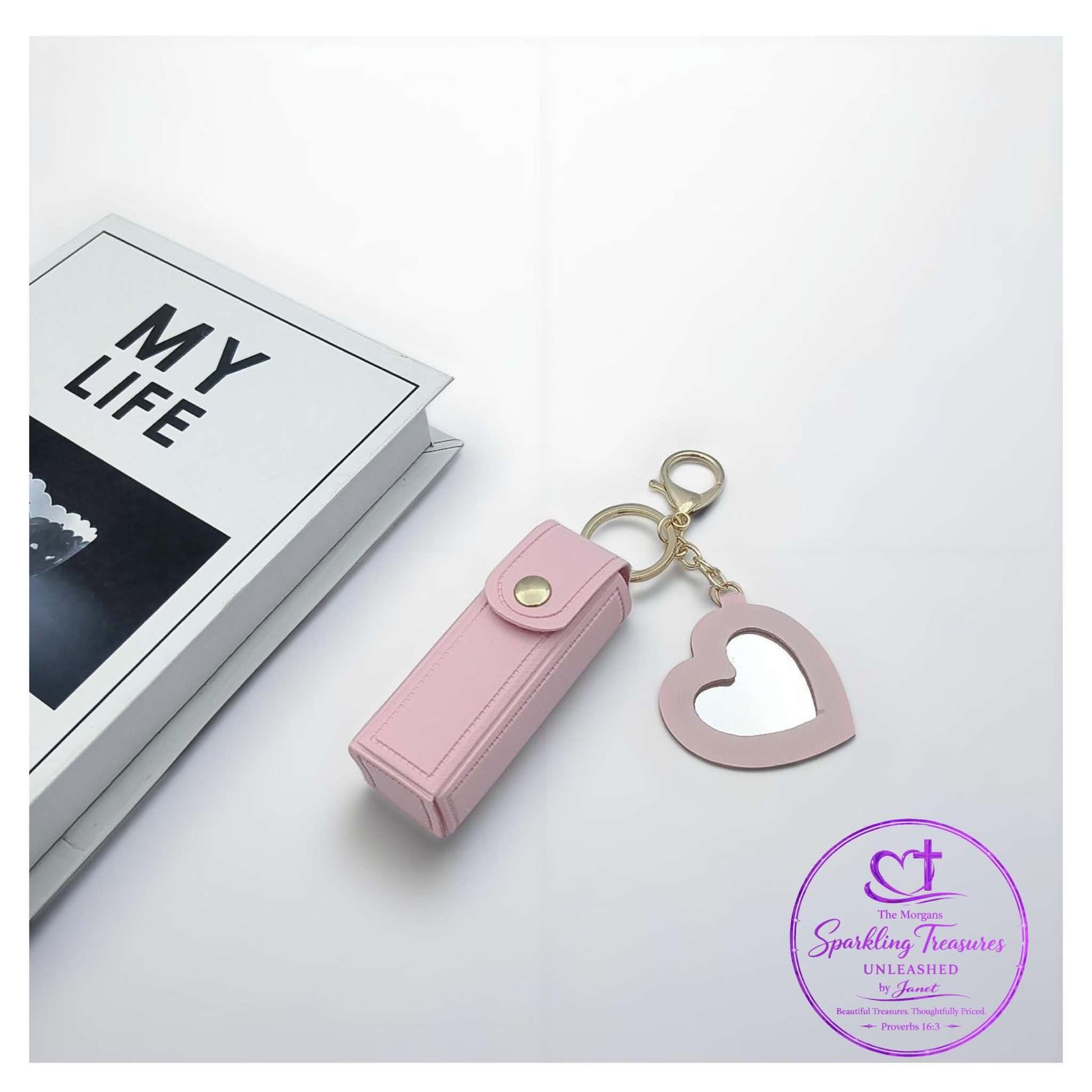 Pink heart-shaped keychain and lip balm case on a white surface with 'My Life' book in the background.