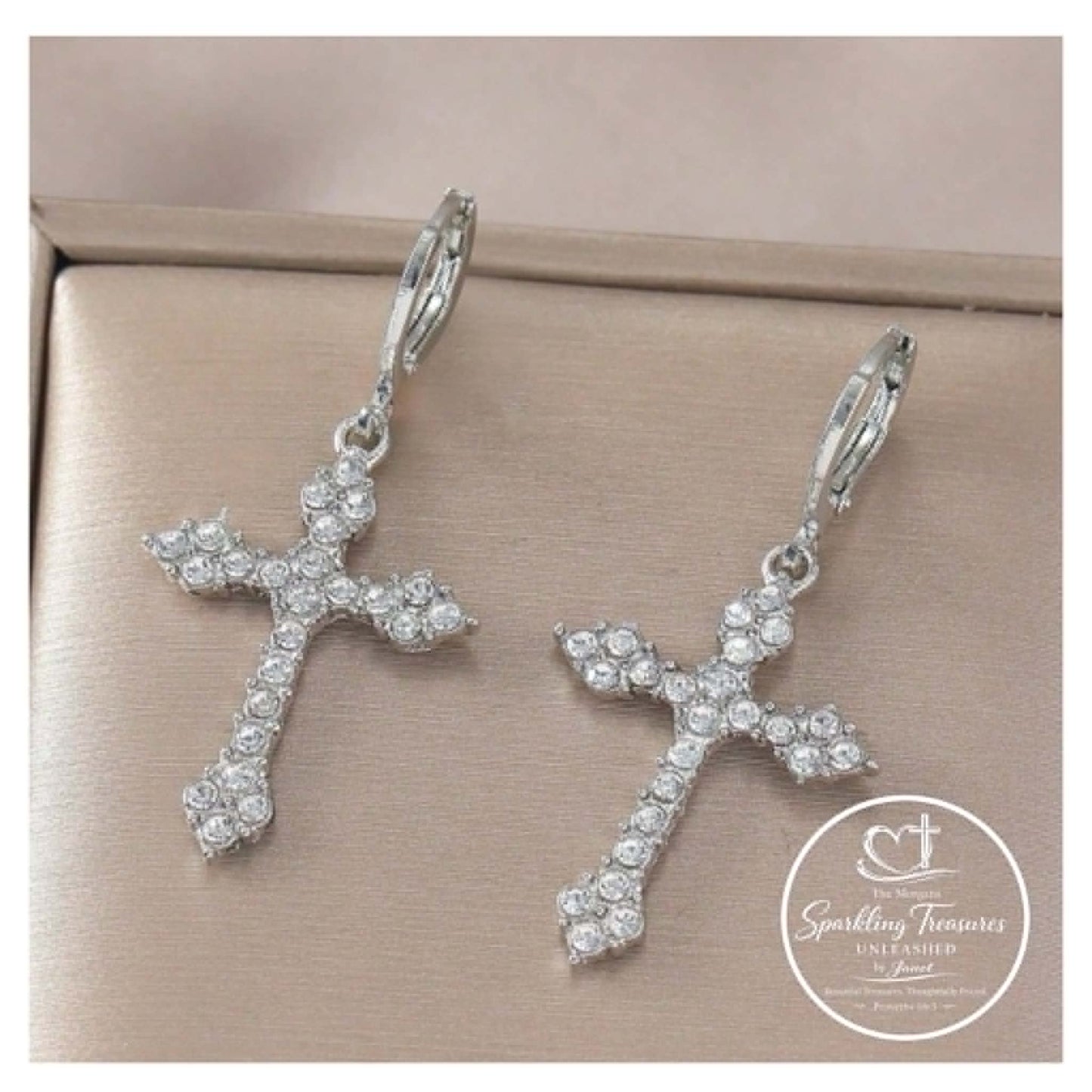 Silver cross-shaped earrings with clear stones on a beige background, featuring 'Sparkling Treasures' logo.