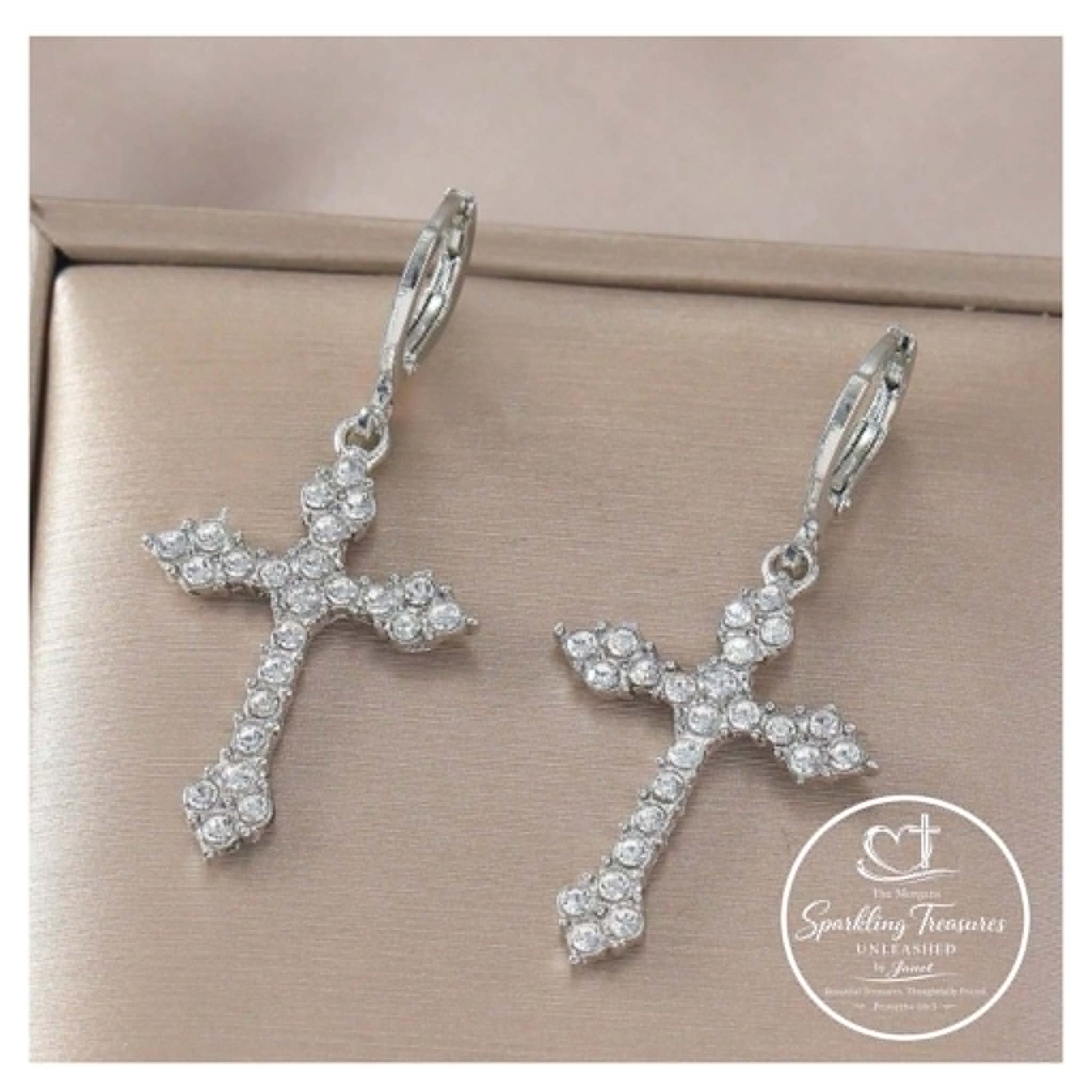 Silver cross-shaped earrings with clear stones on a beige background, featuring 'Sparkling Treasures' logo.