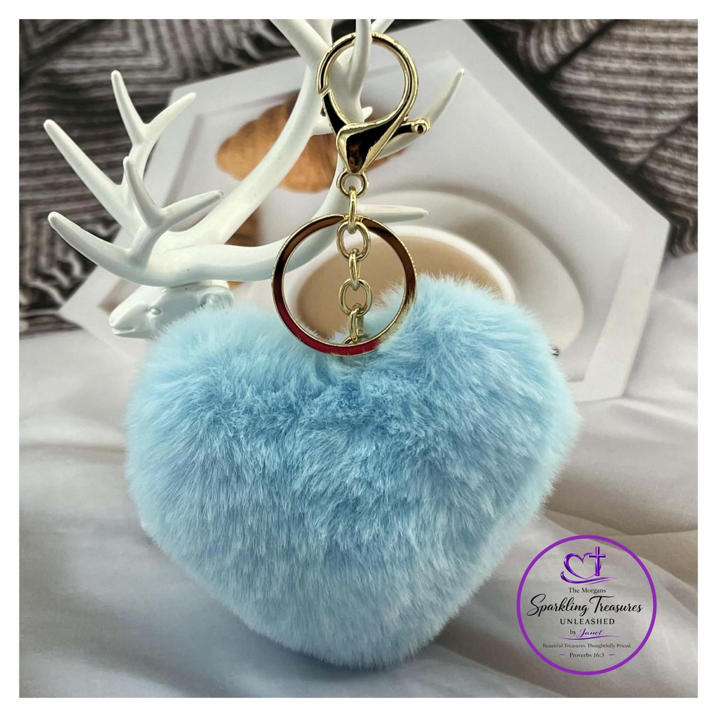Light blue fluffy keychain with gold ring on a white surface with decorative antlers.