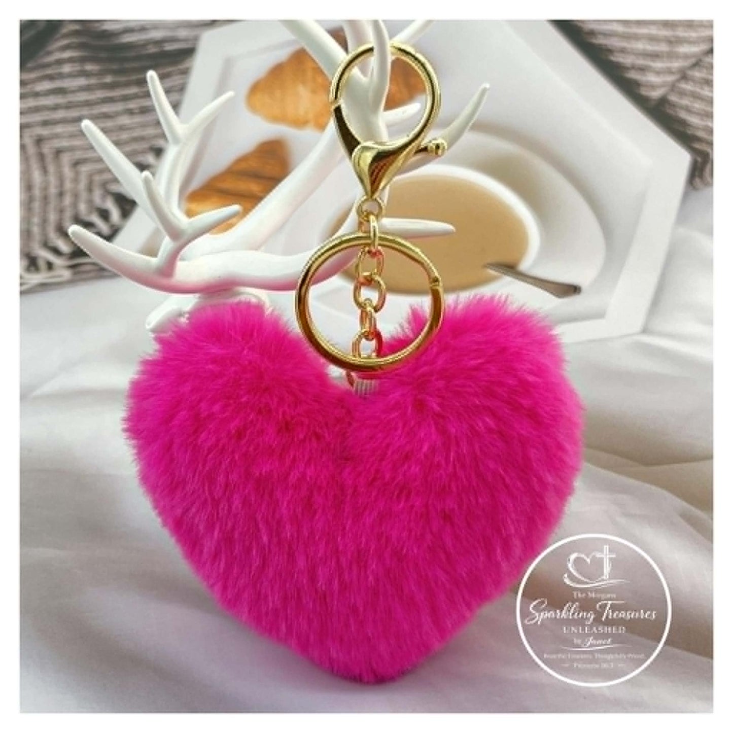 Pink heart-shaped fluffy keychain with gold ring on a white surface.