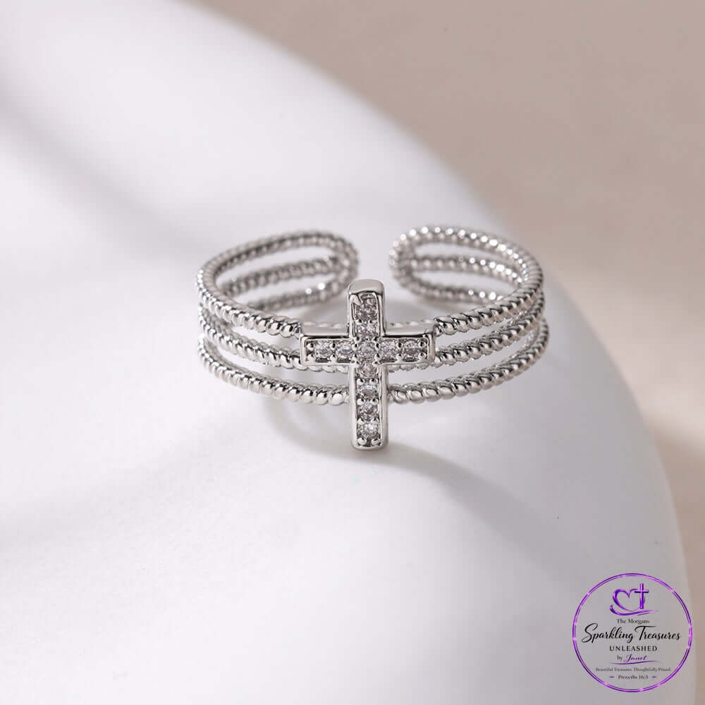 Silver cross ring with rhinestones on a white surface, showcasing its exquisite layered design and sparkle.