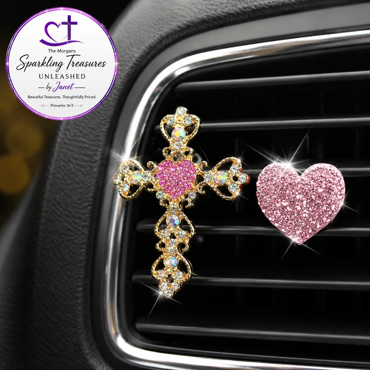 A gold cross-shaped car air freshener ornament with a pink rhinestone heart in the center, shown clipped to a car air vent next to a separate pink glitter heart charm. A circular logo for 'The Morgana Sparkling Treasures Unleashed by Janet' is visible in the top-left corner.