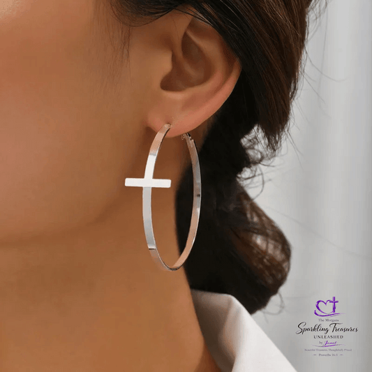 Silver hoop earring with cross design worn by a person, brand logo visible