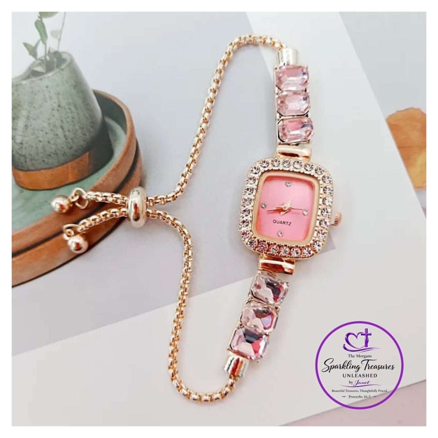 Pink watch with gemstone strap on a white surface, brand 'Sparkling Treasures' visible.