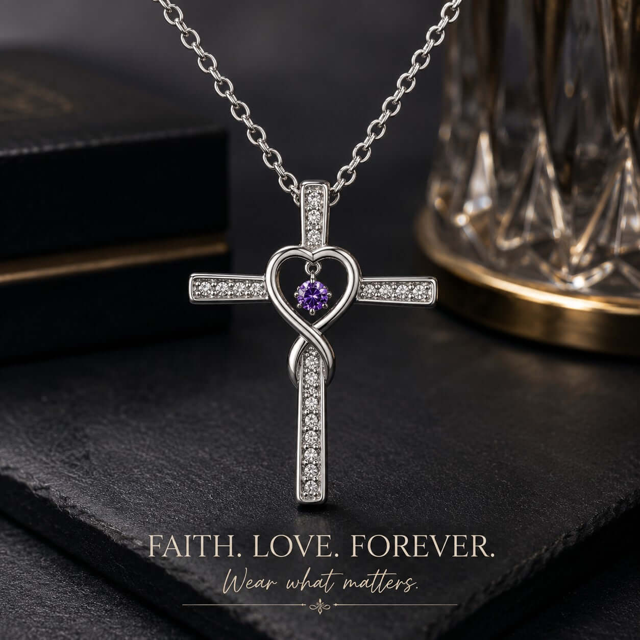 Silver cross necklace with heart design and purple gemstone on a dark surface.