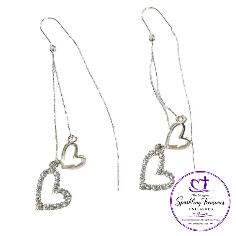 A pair of silver dangle earrings with heart charms, one solid heart and one rhinestone-encrusted heart, shown on a white background with a purple brand logo overlay in the bottom right corner.