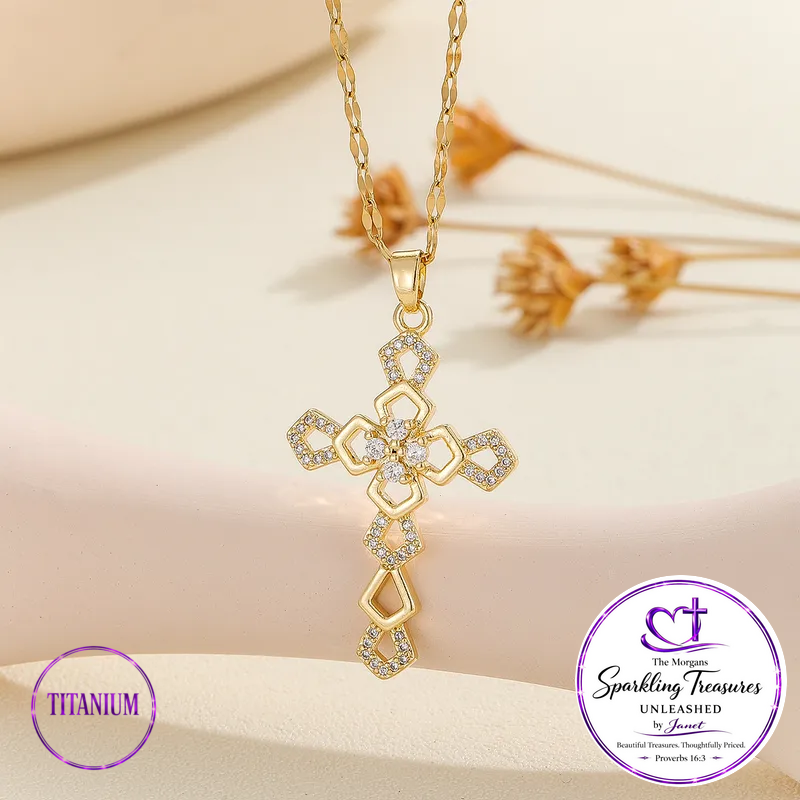 Gold cross pendant necklace with clear stones, displayed on a soft beige surface with dried flowers in the background. Purple circular badges at the bottom read 'TITANIUM' and 'The Mornin Sparkling Treasures UNLEASHED by Anusha'.